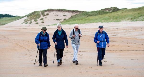 Four older people walking along a beach