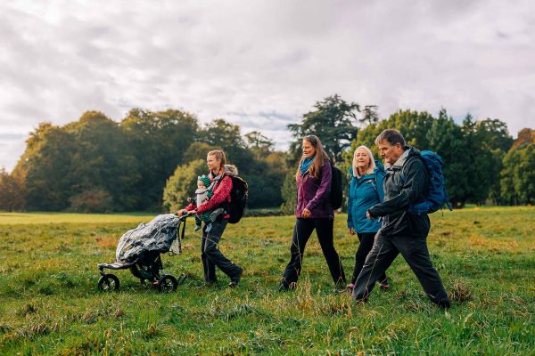 four ramblers and a baby in a pram walking across a field