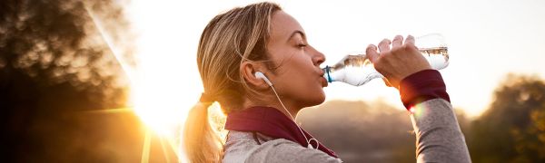 A female athlete drinking water from a bottle with headphones on