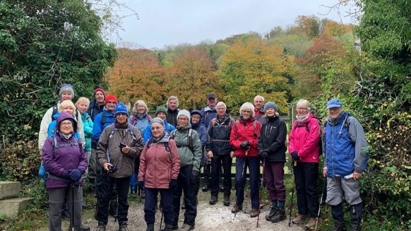 Smiling walkers in a clearing surrounded by autumnal trees.