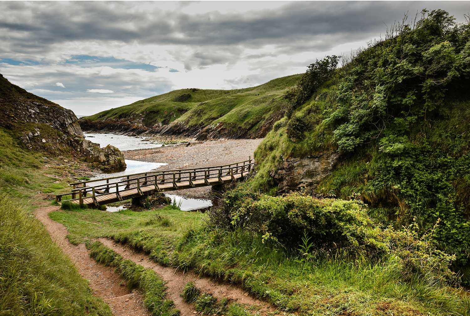 A path leading down to a bridge by a sandy bay