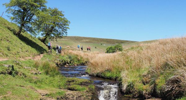 walkers in a shallow valley with a stream running through it.