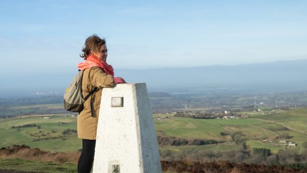 A female walker leaning on a post looking out over a green landscape.