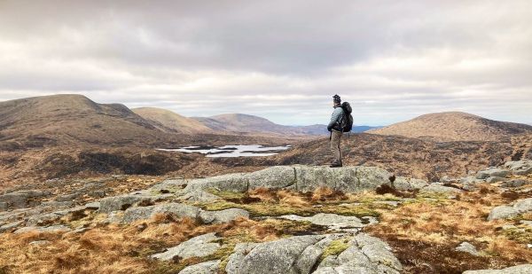 A walker with rucksack standing on rocks in the Galloway National Park.