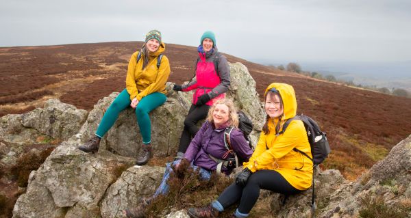 Four walkers sitting on rocks, with hills in the background, smiling into the camera