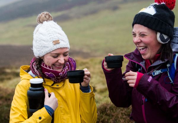 Two women drinking from a flask outdoors