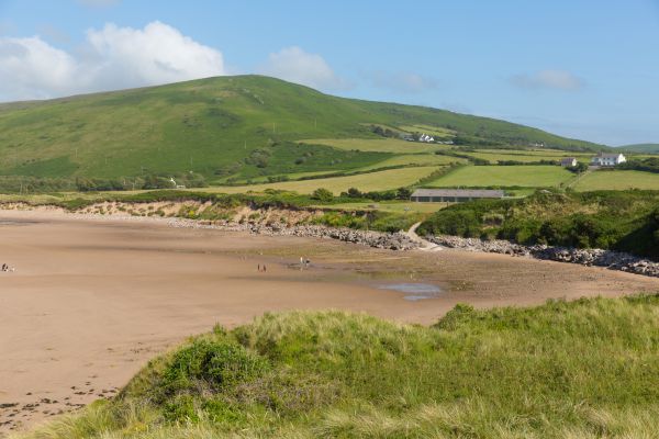 A sandy beach lies underneath an imposing green hill