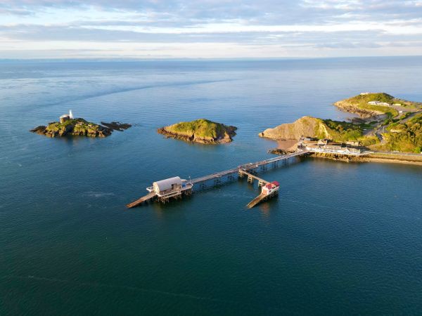 A pier juts out from the headland, just in front of two small islands, one with a white lighthouse