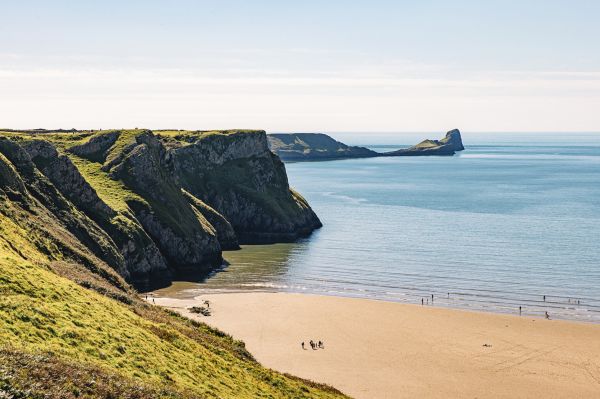 Dramatic cliffs give way to a wide sandy beach and people playing in the breaking waves