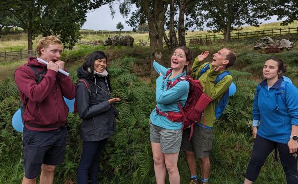 A young group of walkers making scared faces whilst pointing to a bear statue in the bckground.