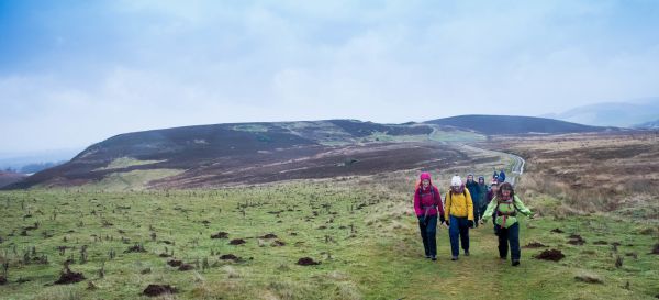 a Ramblers group walking on a grass path with rolling hills in the distance.