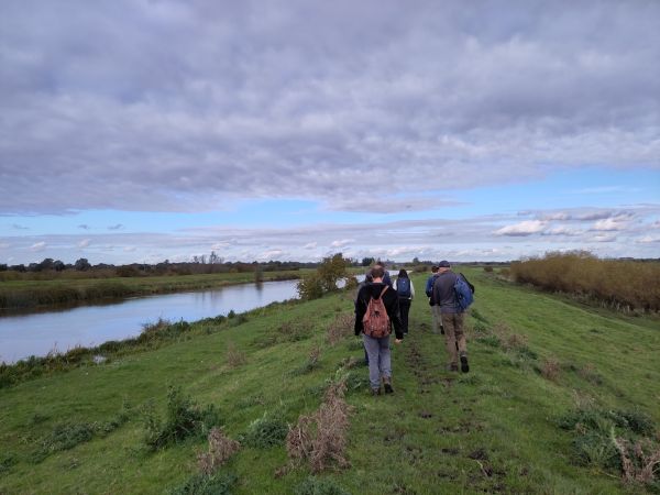 Group walking along the river with Ely Cathedral in the distance