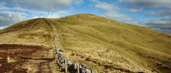 The summit of a big hill with some walkers a long way in the distance