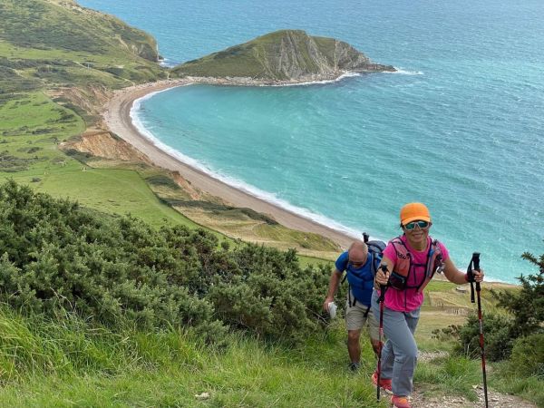 green hill on coast with blue sea curving bay, two people walking up hill on right