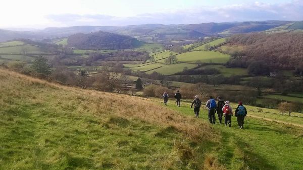 walkers going down a hill with a huge view of a valley in the background