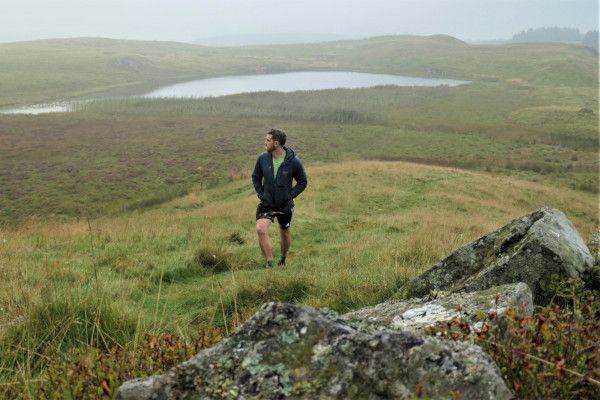 A walker heading up hill on a grassy path away from Lurg loch.