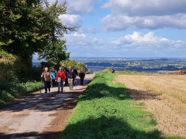 A group of walkers on a wide hilltop path with Norfolk landscape in the background.