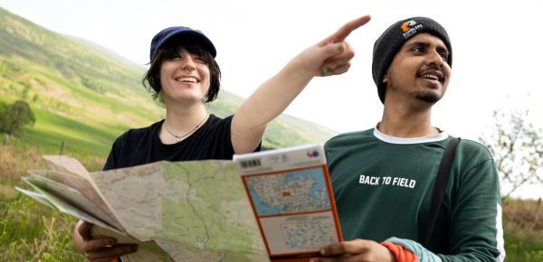 Two young walkers holding a map with one pointing into the distance with hills in the background