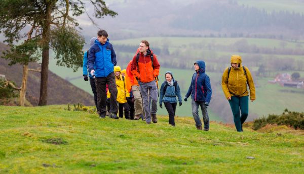 A grop of walkers on a wet day, walking up a hill with rolling hills in the background. 