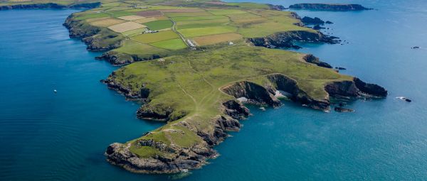 A patchwork of fields gives way to rocky cliffs as a peninsula sticks out into the azure sea