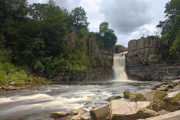 A dramatic waterfull plunges between the rocks into a wide pool, trailing off into rapids in the foreground