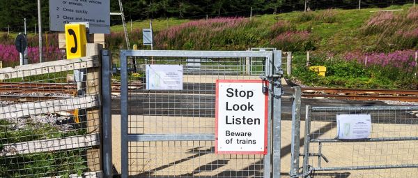 A level crossing showing a locked gate with a stop, look and listen sign.