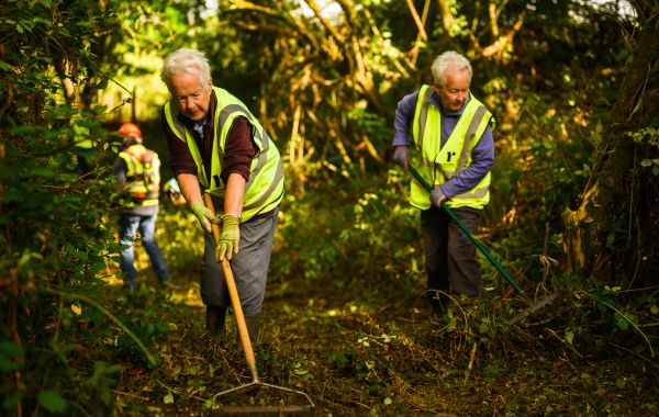 Two Ramblers volunteers in high-vis jackets, rake a pathway.