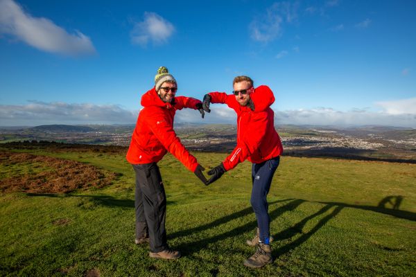 two walkers in red jackets and hiking boots making a heart symbol together.