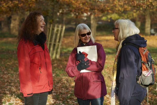 Three women in a park. One is holding a clipboard.