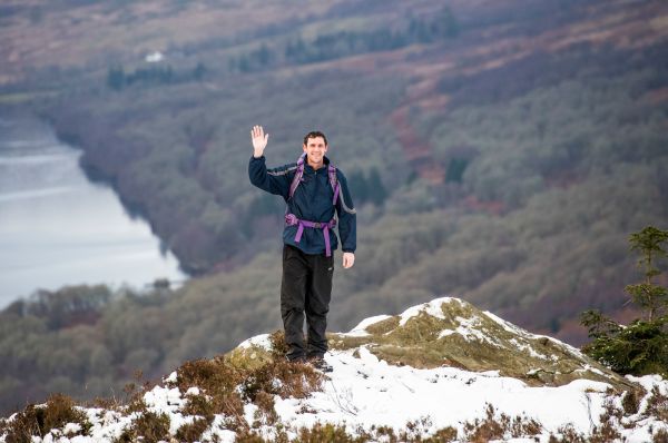 walker waving on a snow-topped hill with dramatic background 