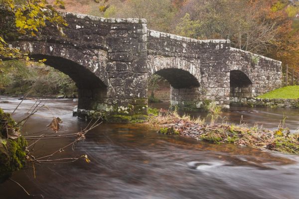 A moss-covered stone bridge runs across a wide brown river