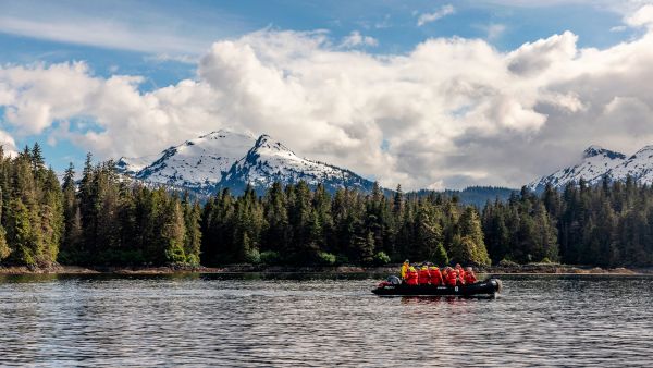 A small boat on a lake with forestry and snowcapped mountains in the background.