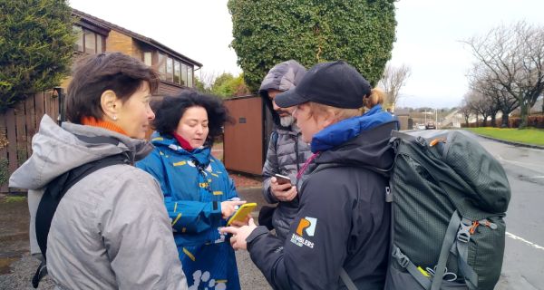 Four walkers consulting phones in an urban setting. 