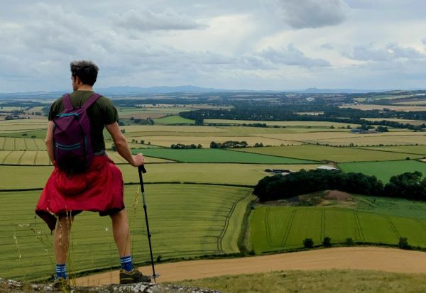 A walker in shorts, with a rucksack and walking pole, looking out over farmland in East Lothian 