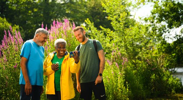 Three walkers smiling into a phone with large plants behind.