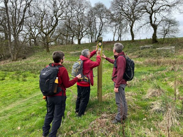 3 walkers with backpacks putting up a waymark with a hammer