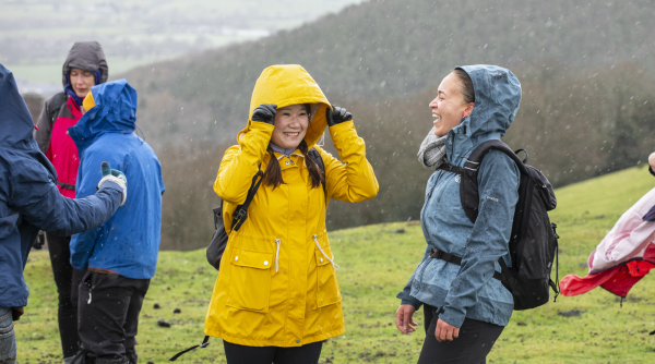 Two walkers smiling in the rain wearing raincoats and carrying backpacks