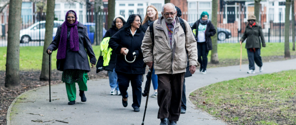 Group walking on paved surface in park, some with walking sticks. 