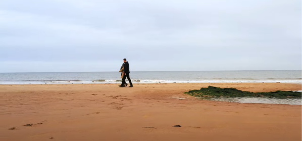 A distant couple, carrying a child walking along the beach next to the sea